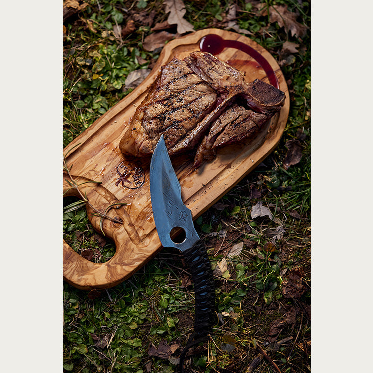 Ispečen odrezak i Predator nož na steak dasci od masllinovog drveta.