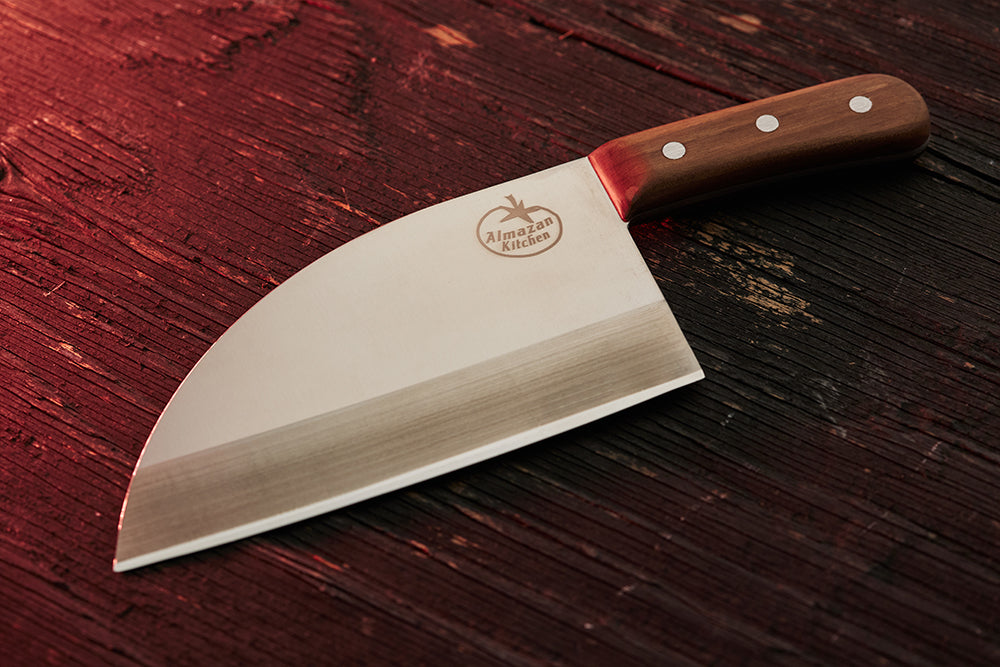 Almazan Kitchen nož od nerđajućeg čelika na drvenom stolu, blago osvetljen crvenim svetlom. 