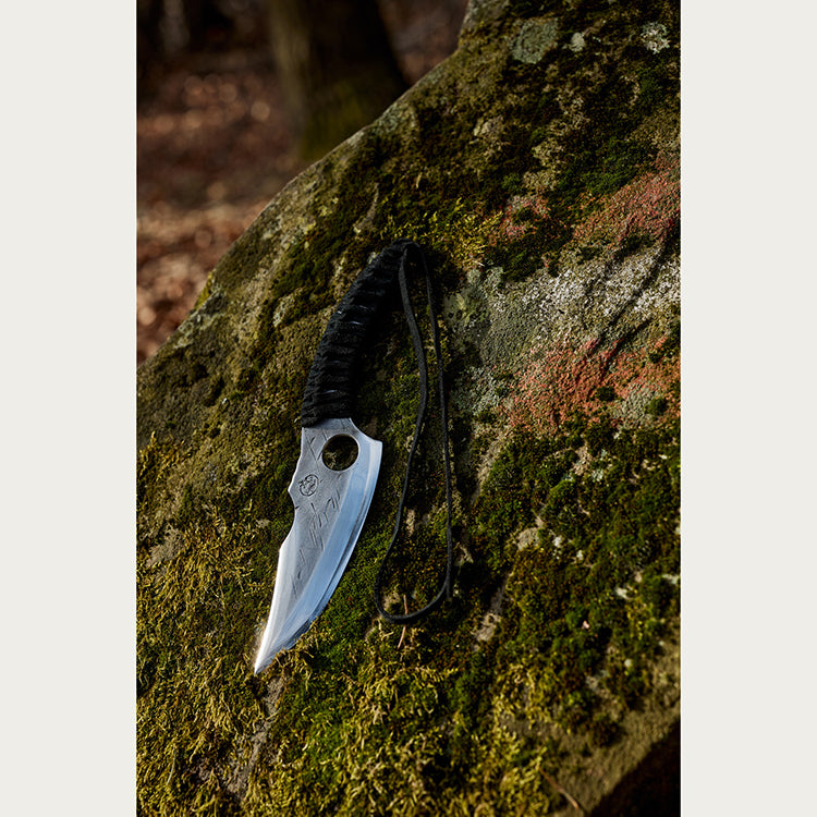 Almazan Kitchen Predator Nož naslonjen na kamen prekriven mahovinom. 