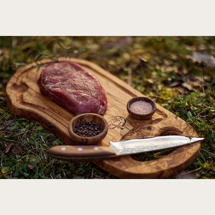 Sirov odrezak, začini i nož od hirurškog čelika na steak dasci od maslinovog drveta. 