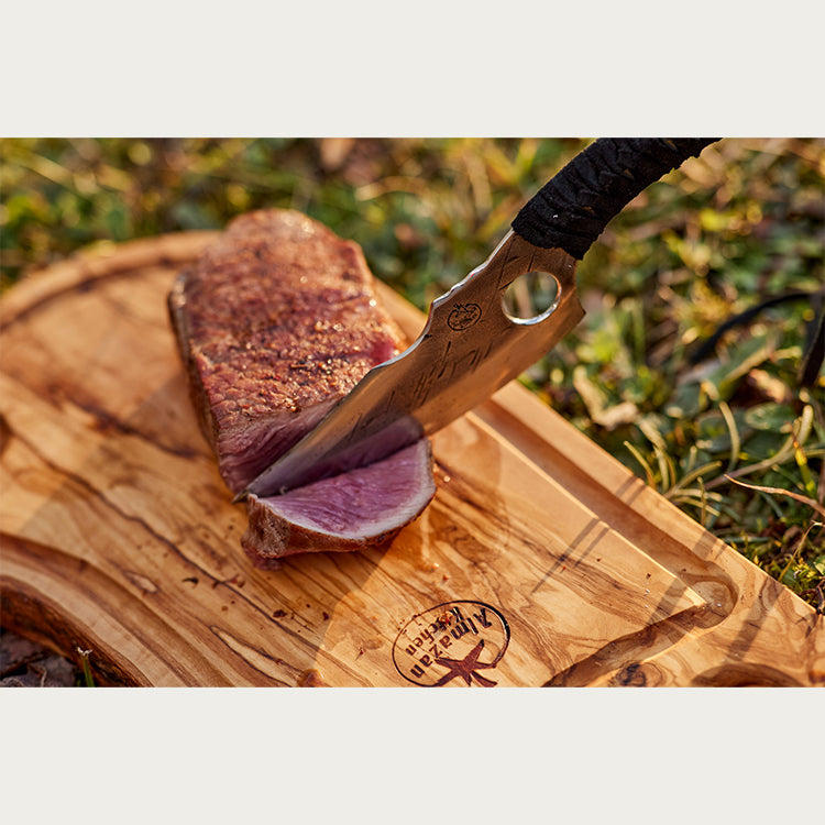 Predator Nož seče komad mesa na dasci za sečenje u prirodi. 