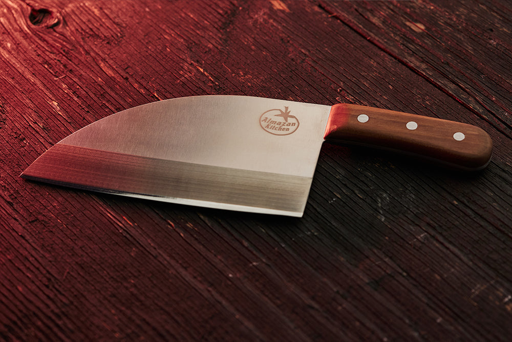 Almazan Kitchen nož od nerđajućeg čelika na drvenom stolu, blago osvetljen crvenim svetlom.