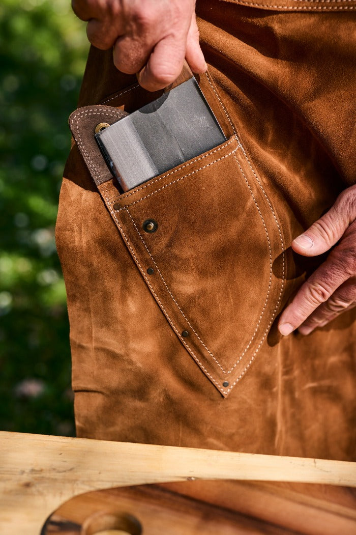 Osoba izvlači kuvarski nož iz džepa na kožnoj kecelji. 