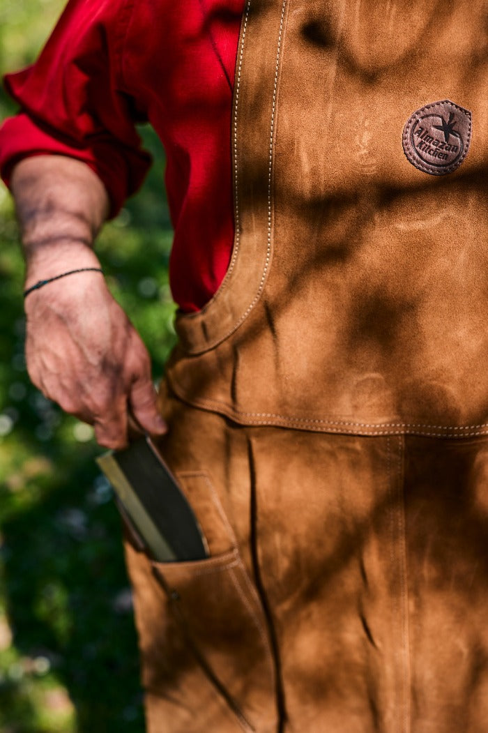 Osoba, obasjana suncem, izvlači kuvarski nož iz džepa na kožnoj kecelji.