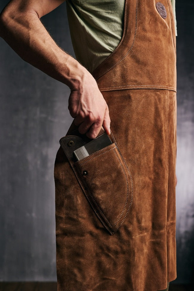 Osoba izvlači kuvarski nož iz posebnog džepa na Almazan Kitchen kožnoj kecelji.